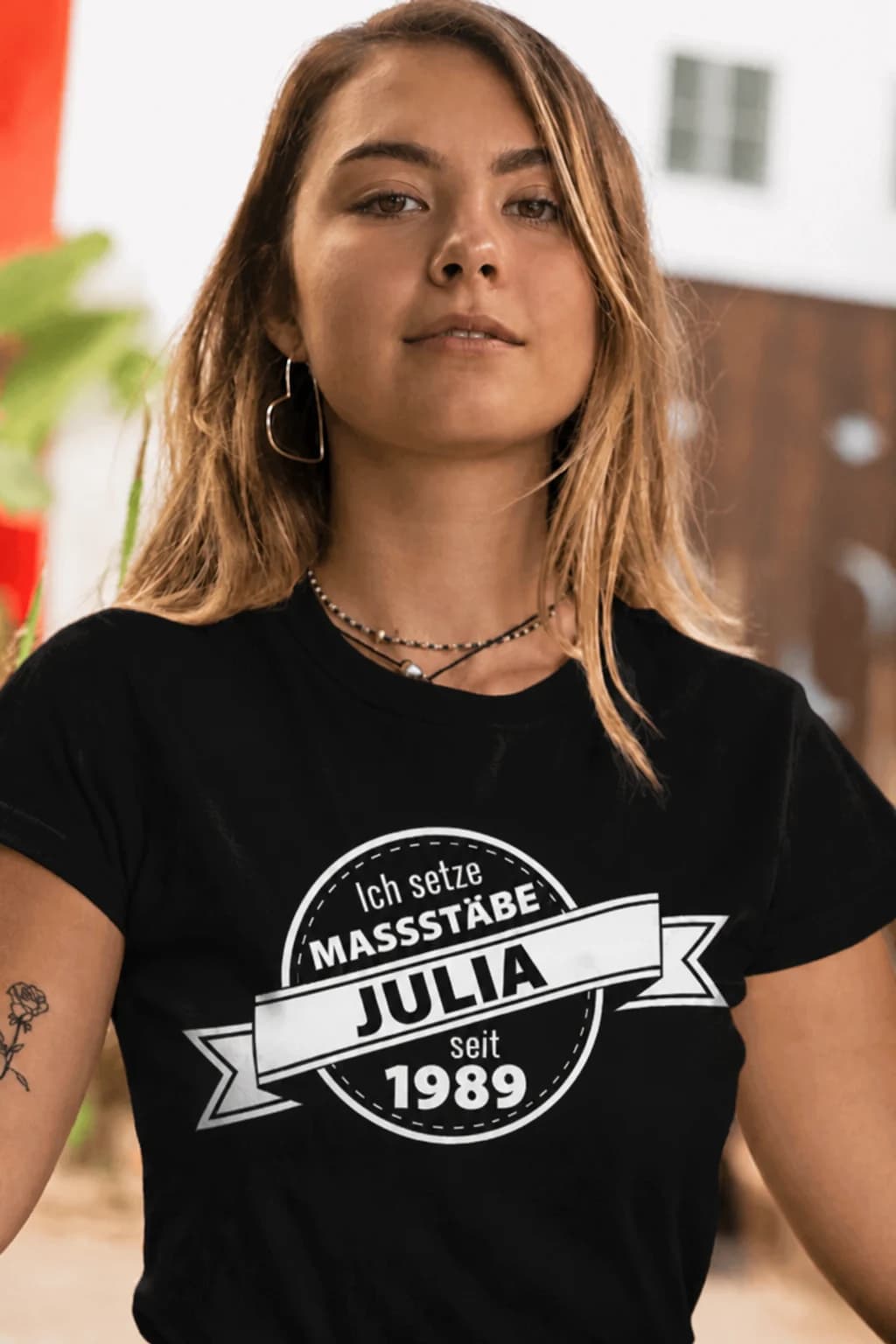 Frau im schwarzen T-Shirt mit Retro-Abzeichen „Ich setze Maßstäbe – Julia – seit 1989“